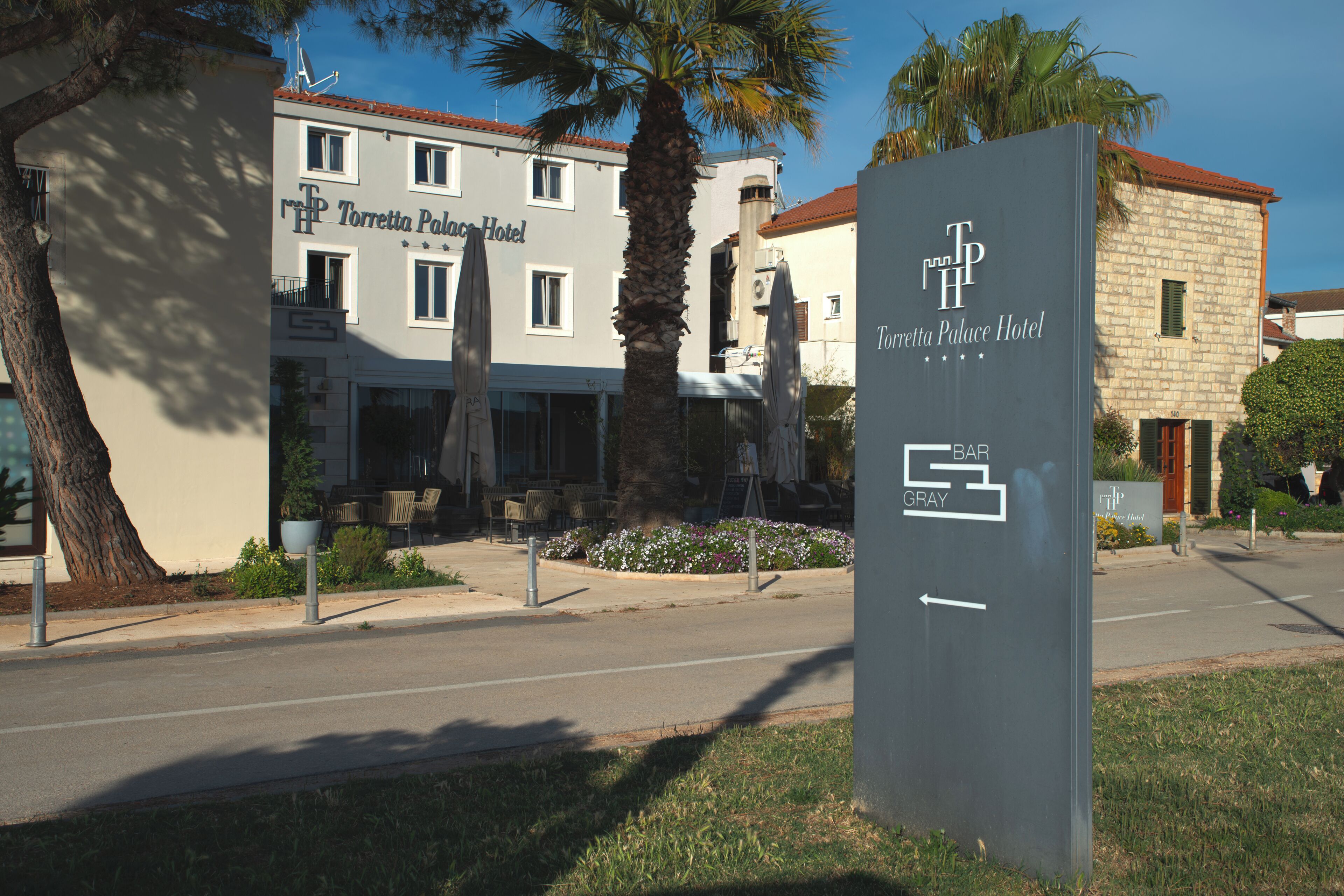 Schild für das Torrette Palace Hotel, mit freiem Blick auf das Gebäude und einer Palme im Vordergrund.