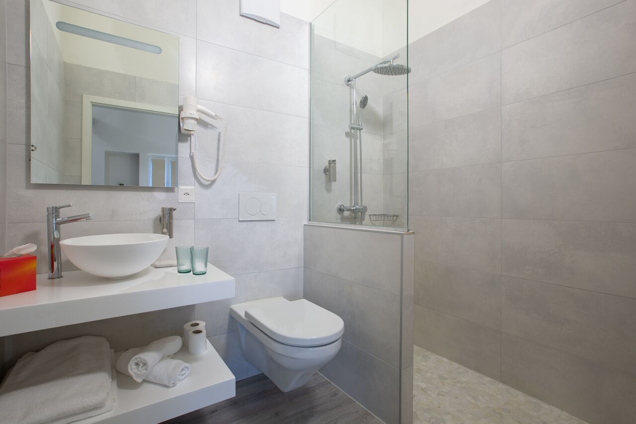 Une salle de bain moderne avec un grand lavabo blanc, des toilettes, une douche en verre et un miroir au-dessus du lavabo.