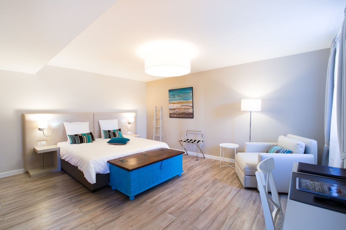 Un dormitorio moderno con cama, un reposapiés azul, un sofá blanco, un escritorio y un cuadro en la pared.