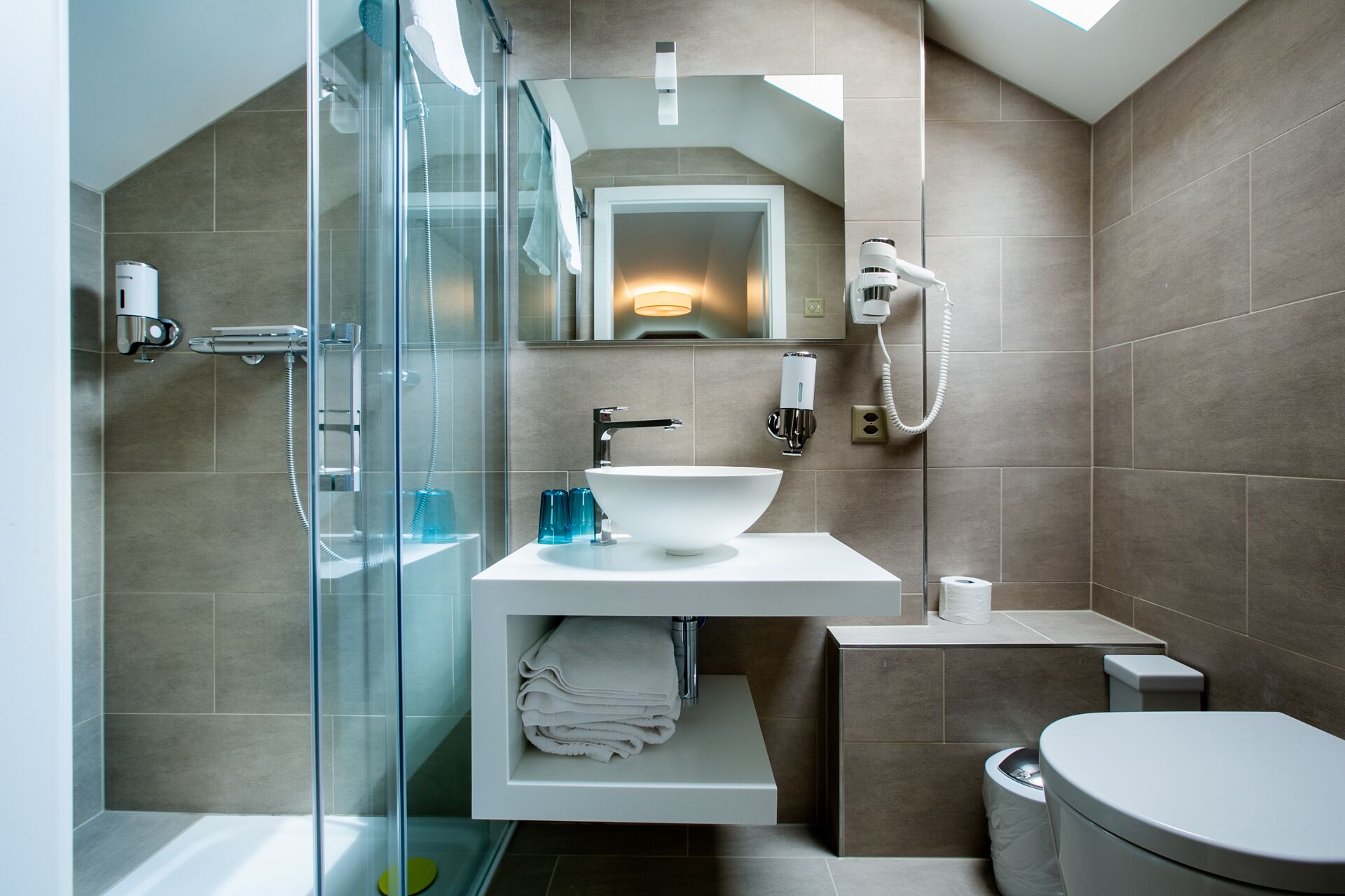 Een moderne badkamer met een douchecabine van glas, een witte wastafel en een toilet.