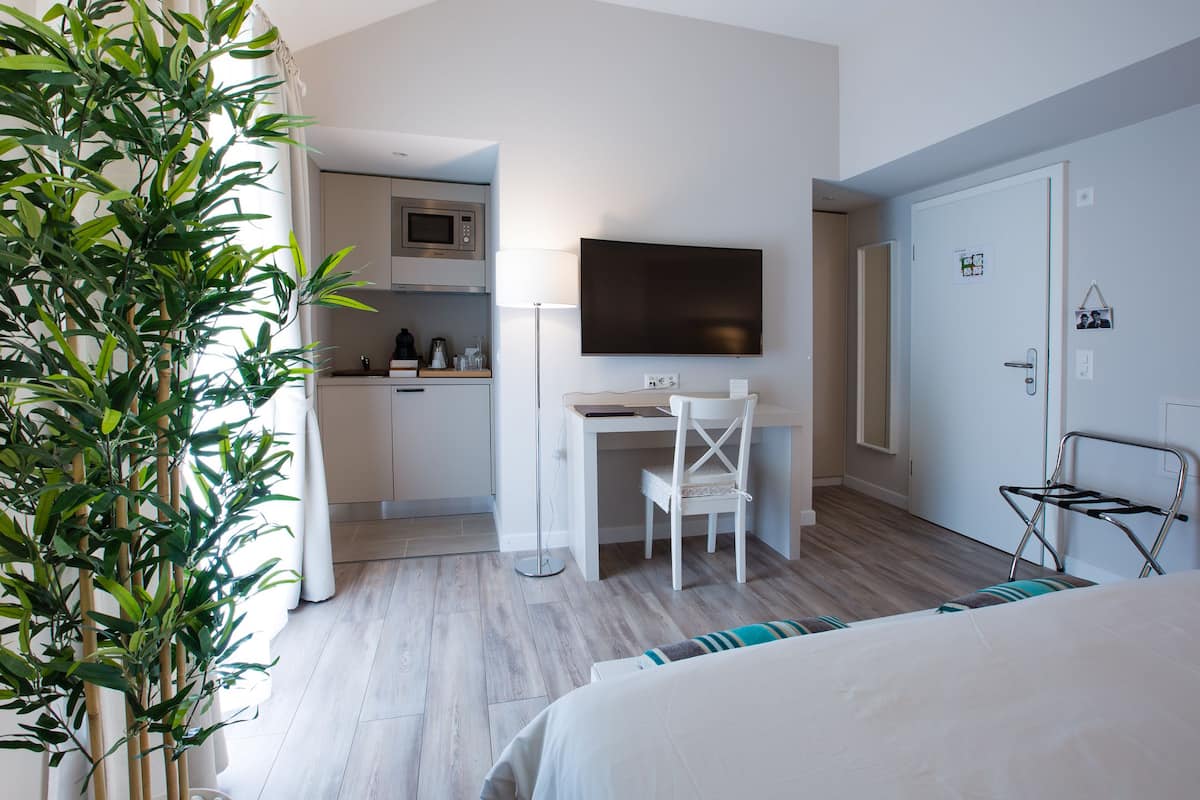 Habitación de hotel con cama, escritorio y silla, televisor, microondas, pequeña cocina y una planta en maceta.
