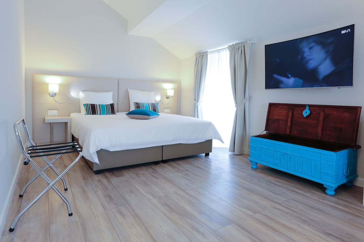 Habitación de hotel con cama, mesitas de noche, televisor, suelo de madera y un aparador azul.