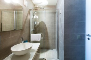Un baño moderno con ducha de vidrio, lavabo blanco de cuenca grande y espejo sobre el lavabo.
