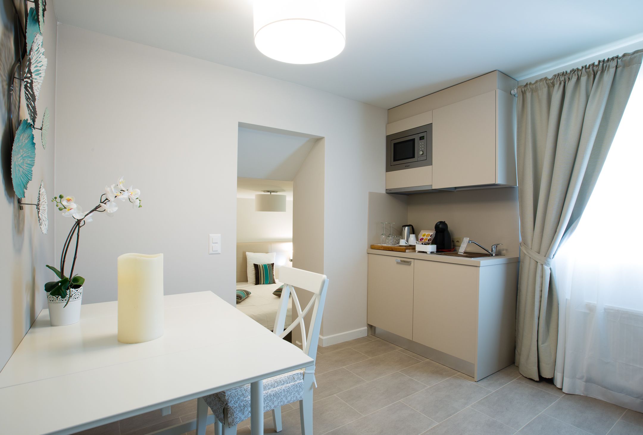 A compact kitchen with a microwave, a sink, and a small countertop. There's a dining table with chairs and a potted plant.
