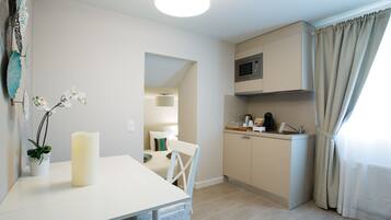 A compact kitchen with a microwave, a sink, and a small countertop. There's a dining table with chairs and a potted plant.