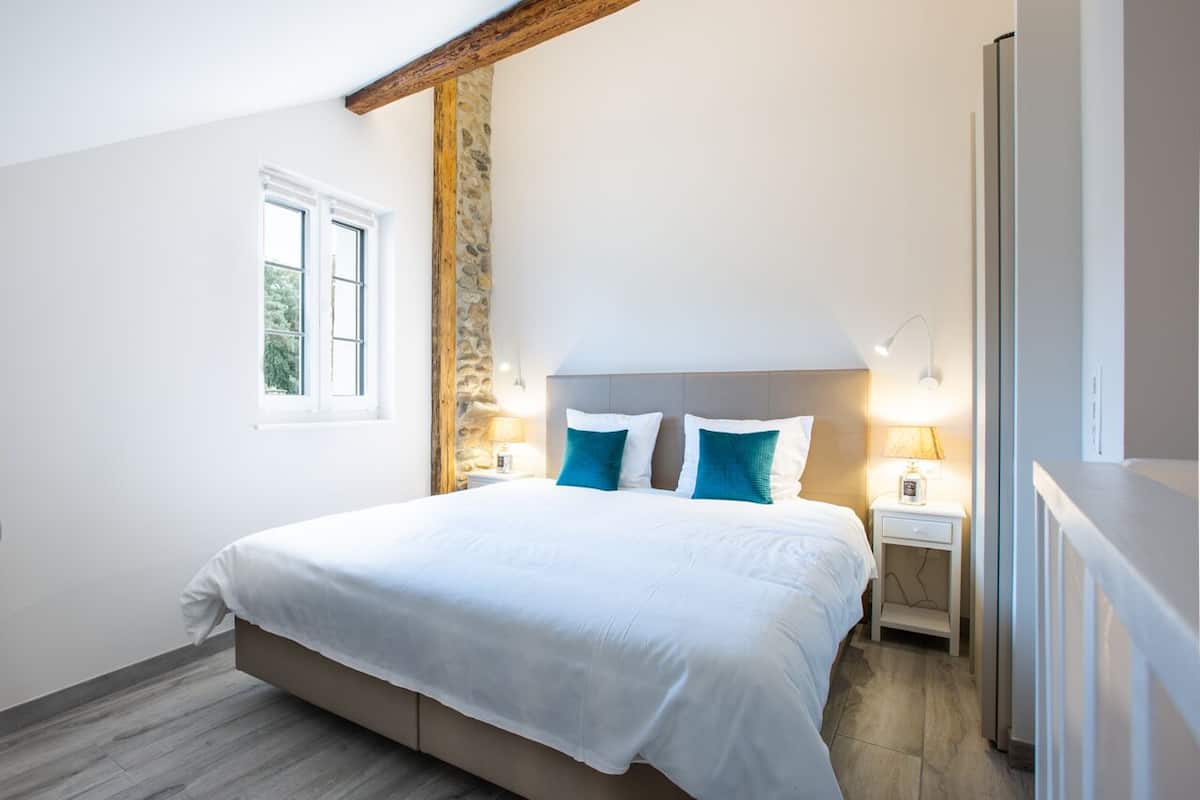 Un dormitorio con una cama grande, dos mesitas de noche con lámparas, una pared de piedra y una ventana.