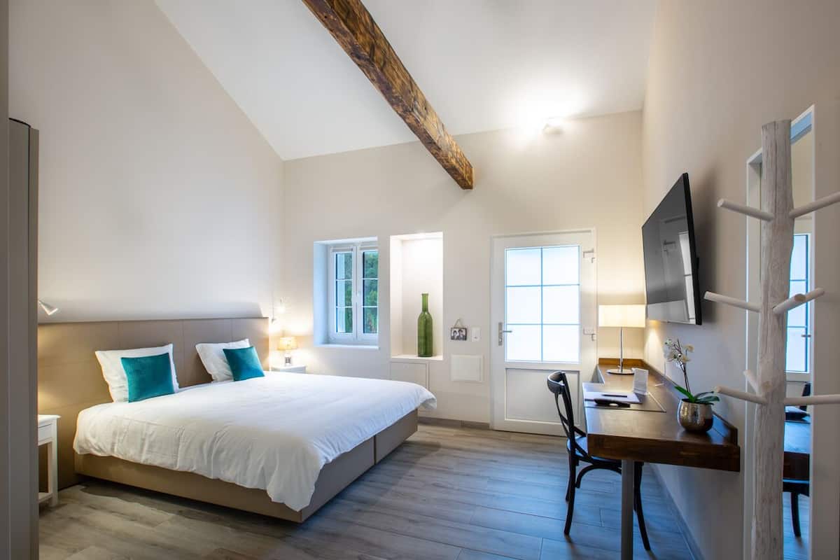 Un dormitorio con cama, mesitas de noche, un escritorio con silla, televisor y ventana.