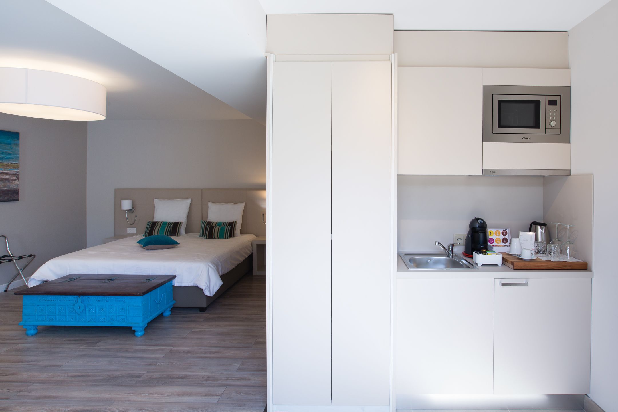 Una habitación de hotel compacta con una cama, una kitchenette pequeña y un aparador azul.