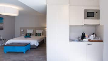 Una habitación de hotel compacta con una cama, una kitchenette pequeña y un aparador azul.