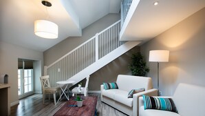 A spacious living area with a staircase, a white sofa, a wooden coffee table, and a floor lamp.
