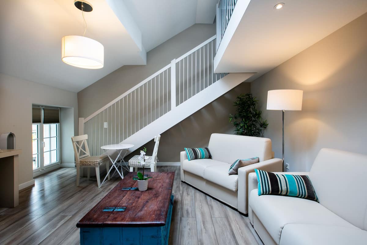 Amplia sala de estar con una escalera, un sofá blanco, una mesa de centro de madera y una lámpara de pie.