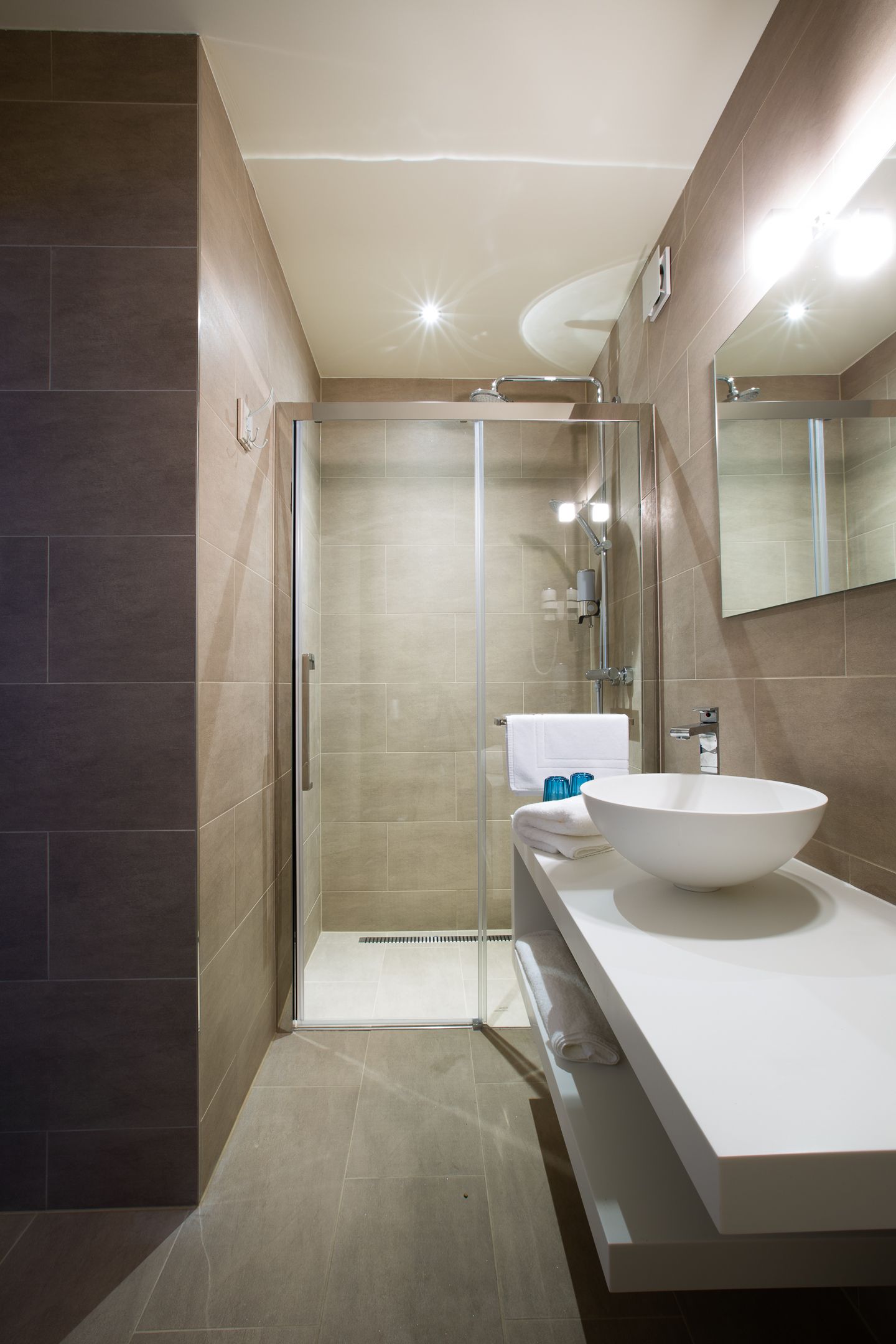 A modern bathroom with a glass shower enclosure, a large white sink, and a mirror above the sink.
