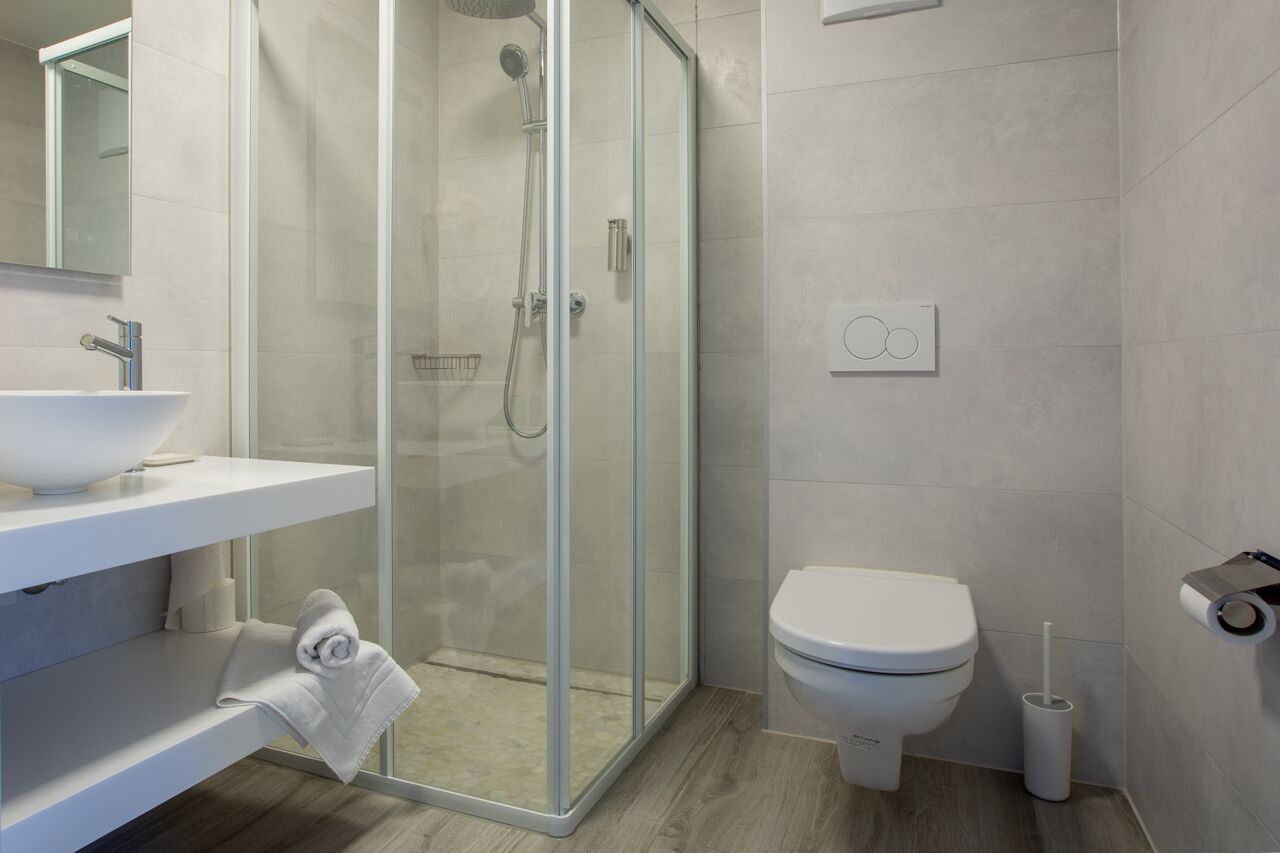 Un baño moderno con ducha de vidrio, lavamanos blanco y inodoro.