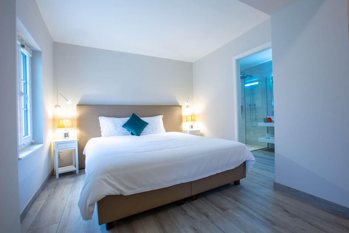 Habitación de hotel moderna con una cama grande, lámparas de noche, una mesita de noche y vistas al baño.