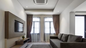 A modern living room with a flat-screen TV mounted on the wall, a grey sofa, and a small plant on a console table. - Macallum Central Hotel Managed By The Ascott Limited (George Town)