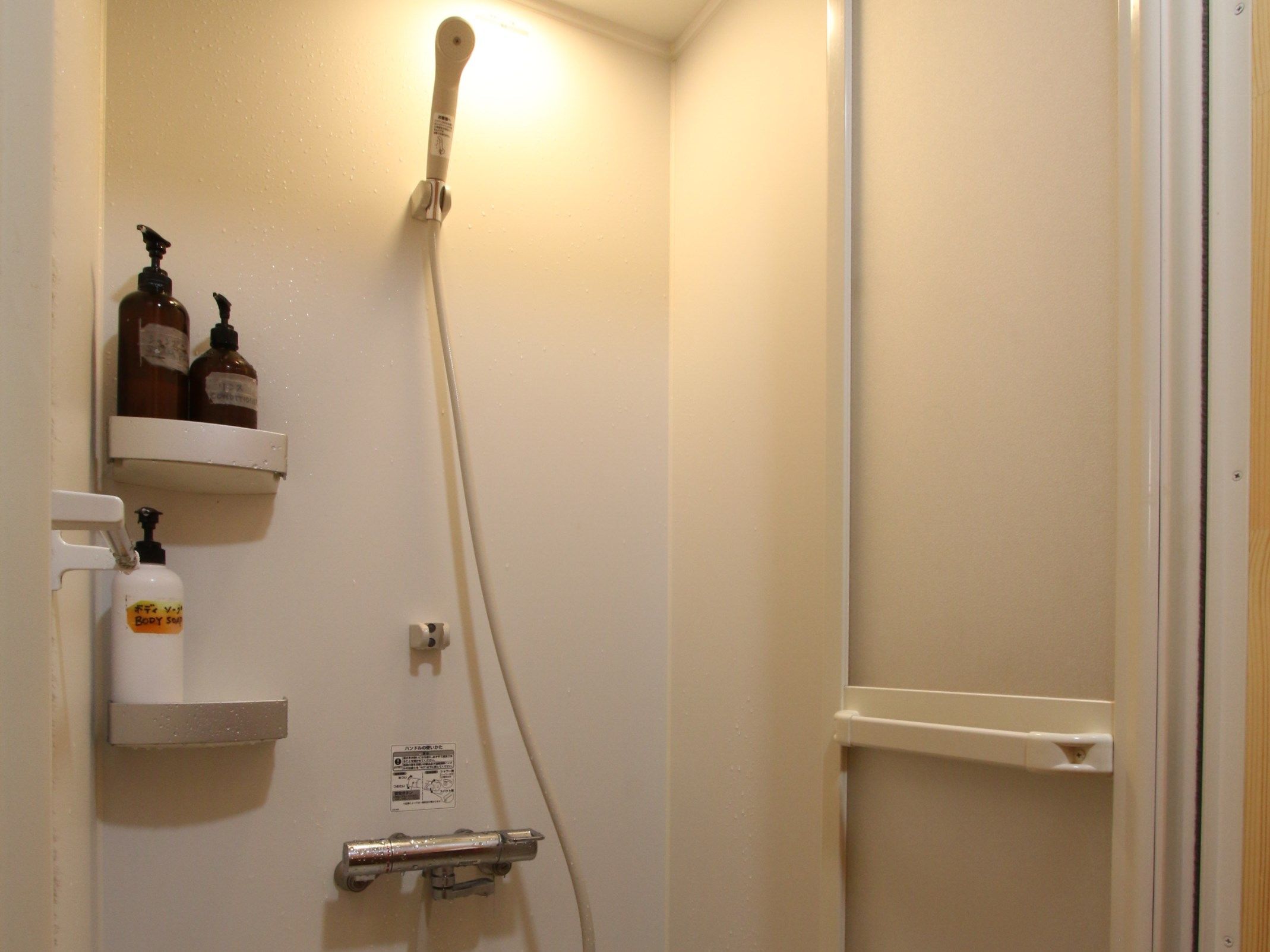 A bathroom with a shower, a soap dispenser, and a bottle of body soap on a shelf.