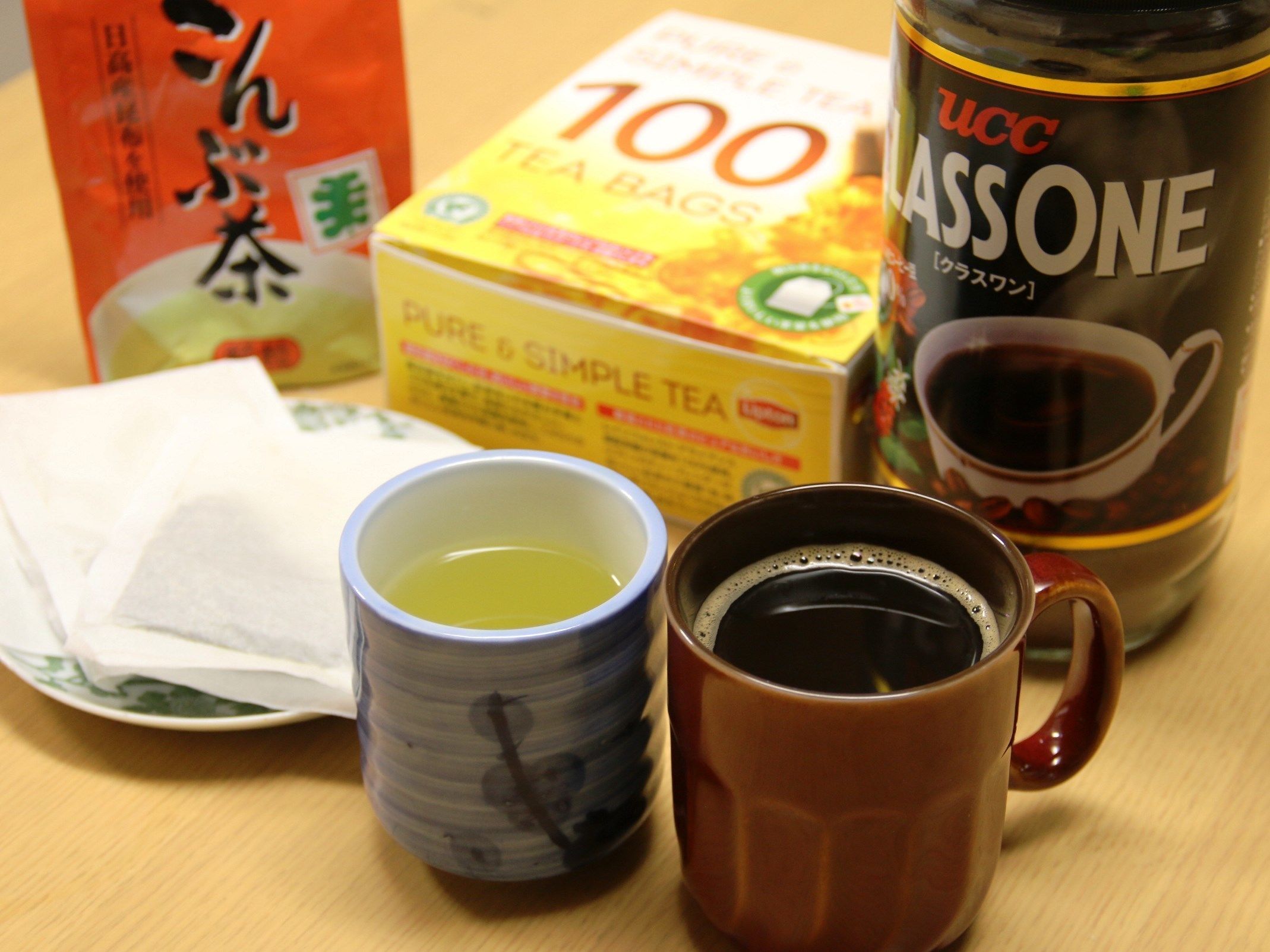 A table with a tea bag box, a coffee container, and two cups.