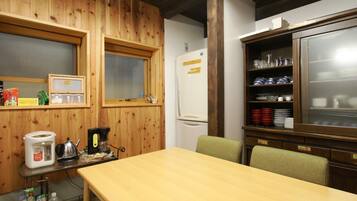 A wooden-paneled room with a wooden table, chairs, a refrigerator, a shelf with dishes, and a window.
