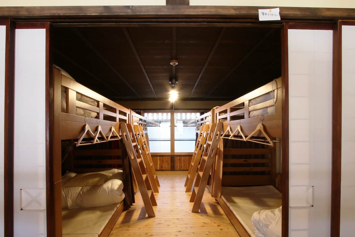 A dormitory room with bunk beds, wooden floors, and a window with a view.