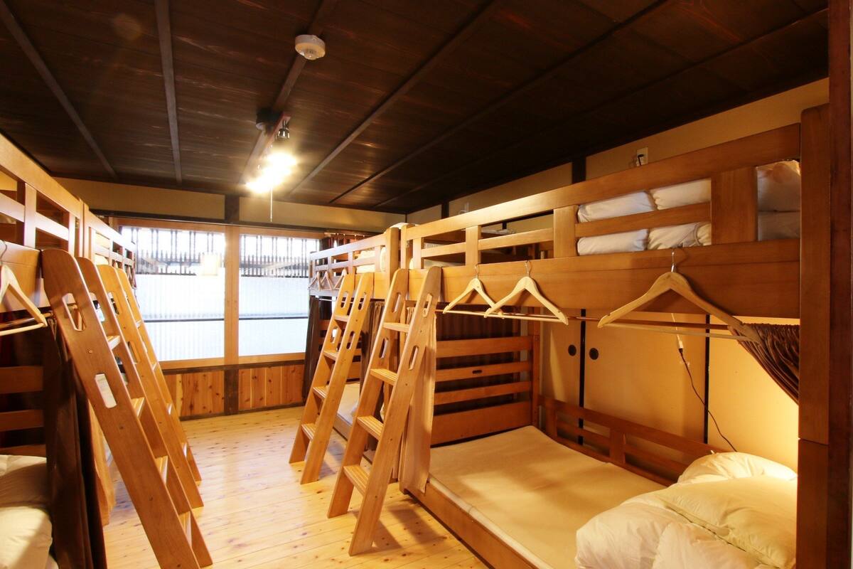 A wooden bunk bed room with a wooden floor, a ceiling light, and a window with curtains.