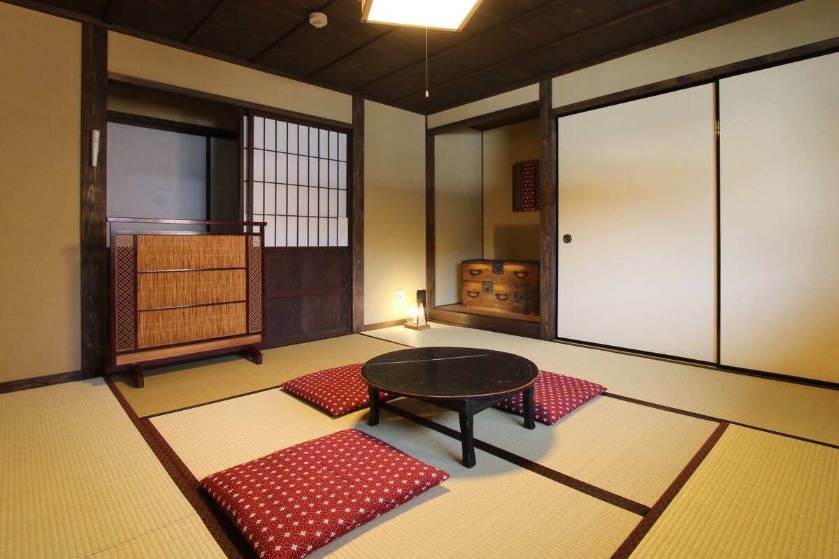 A tatami mat room with a low table and cushions, wooden sliding doors, and a traditional Japanese-style lamp.