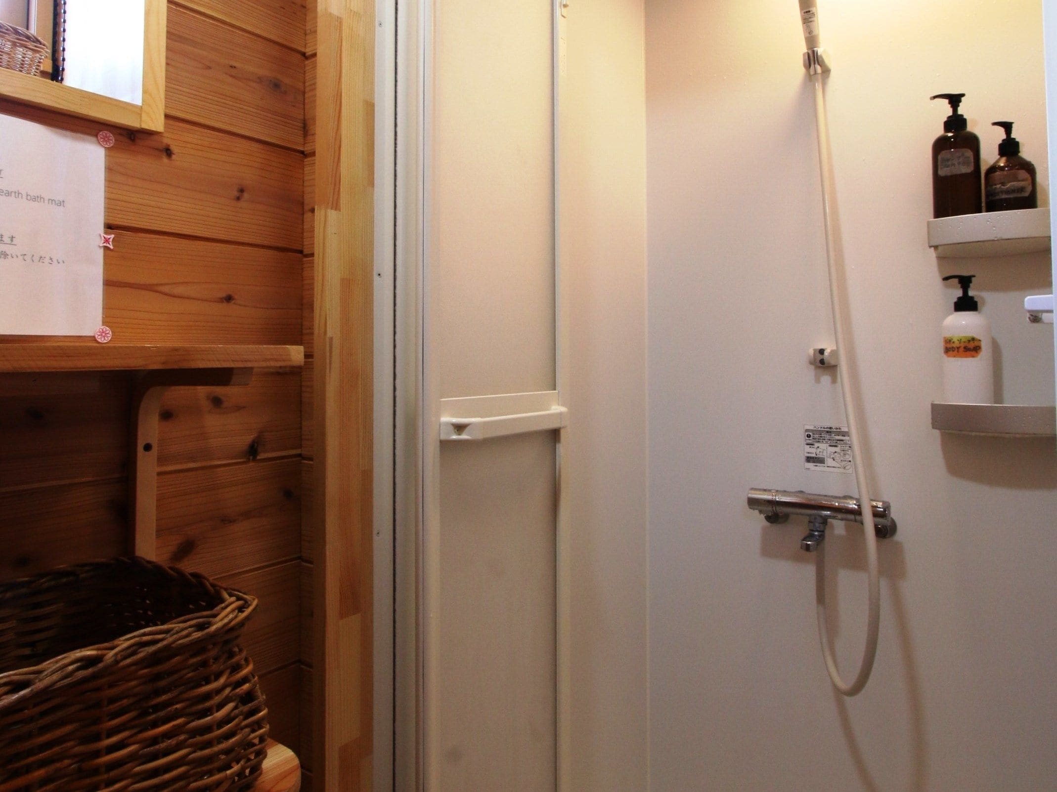A shower area with a white door, a wooden wall, and a shelf with toiletries.