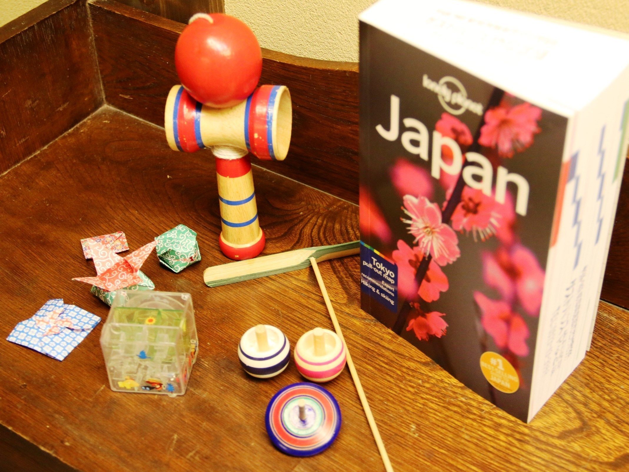 Ett träbord med en utdragbar karta med japanskt tema, en leksak i trä, origamikonst och en plastbehållare.