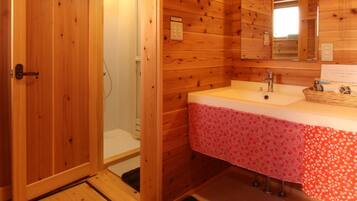 Un baño rústico en una cabaña de madera, con lavamanos, espejo y ducha.