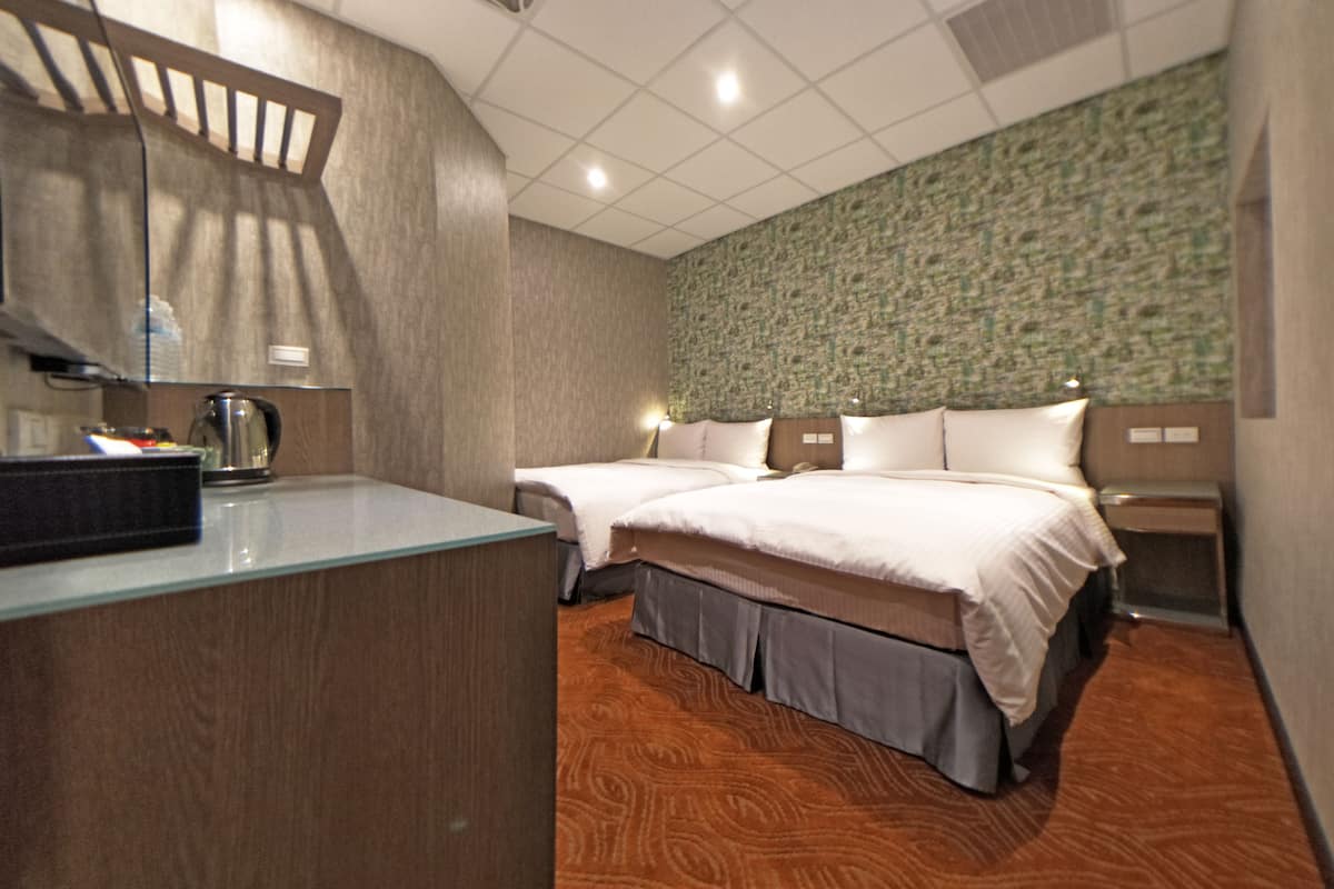 A hotel room with a wooden desk, two beds, a green textured wall, and a patterned carpet.