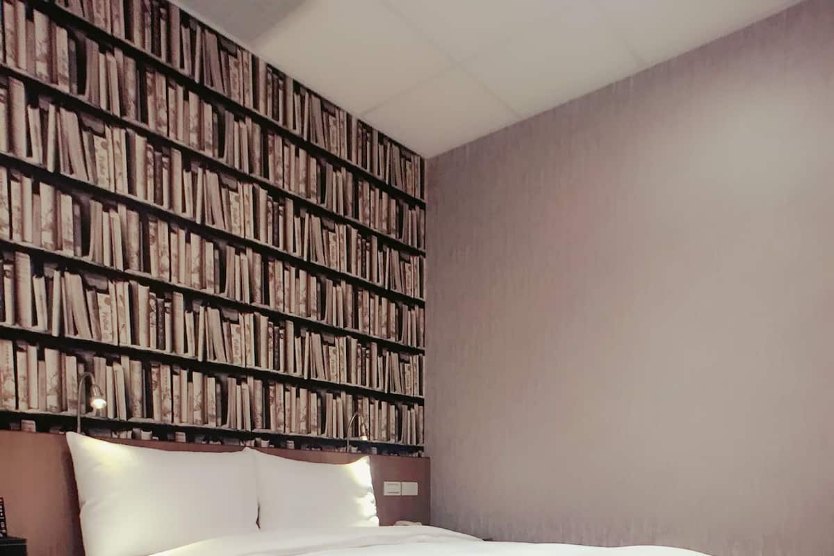 A hotel room with a large bed, a bookshelf, and a nightstand.