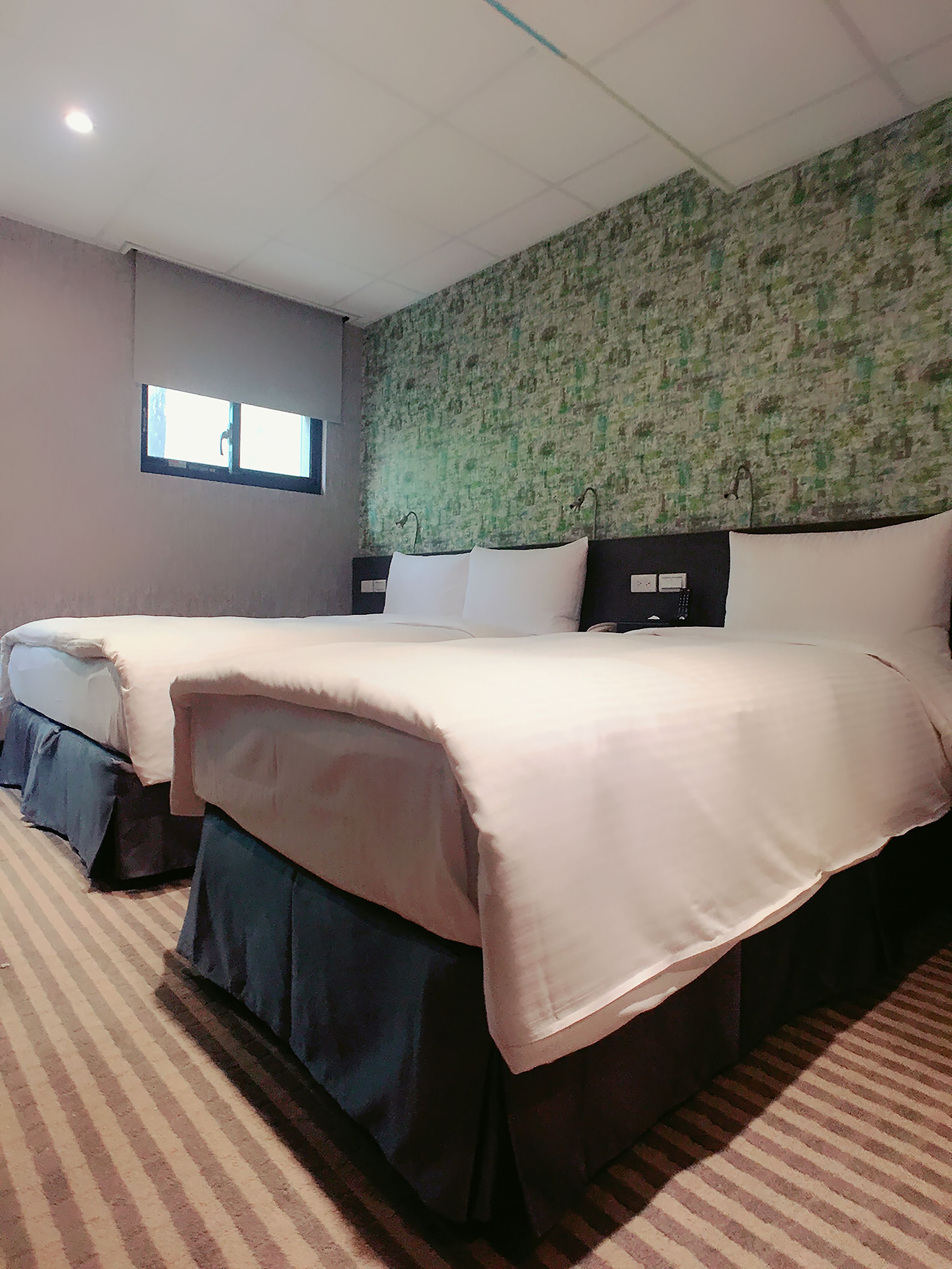A hotel room with two beds, a window, and a green textured wall.
