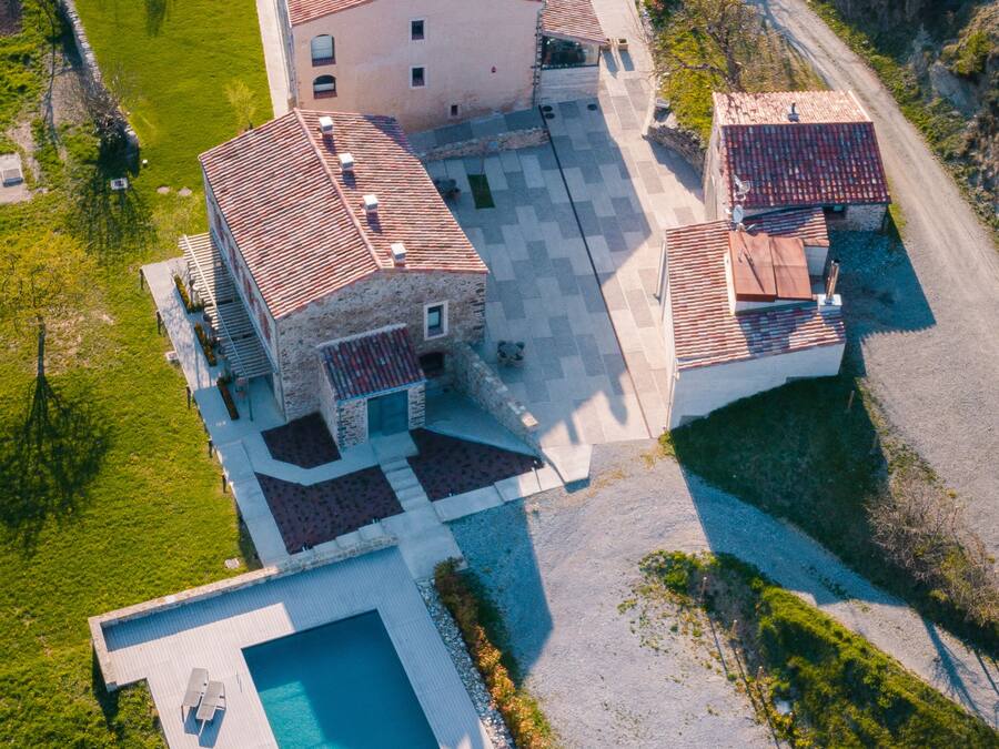 An aerial view of a property with a swimming pool, a large building with a tiled roof, and a smaller adjacent structure.