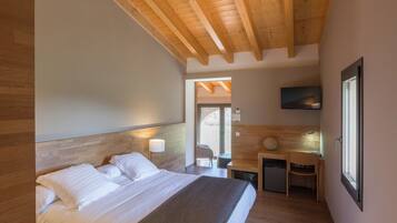 Un dormitorio con cabecera de madera, cama con sábanas blancas, un escritorio con silla, un refrigerador pequeño y un televisor montado en la pared.