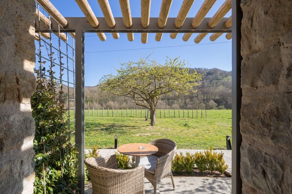 Un patio con sillas de mimbre y una mesa, con vistas a un campo cubierto de césped y un árbol.