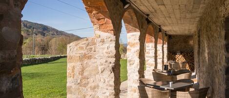 Un patio al aire libre con arcos de piedra, muebles de mimbre y vistas a un paisaje verde.