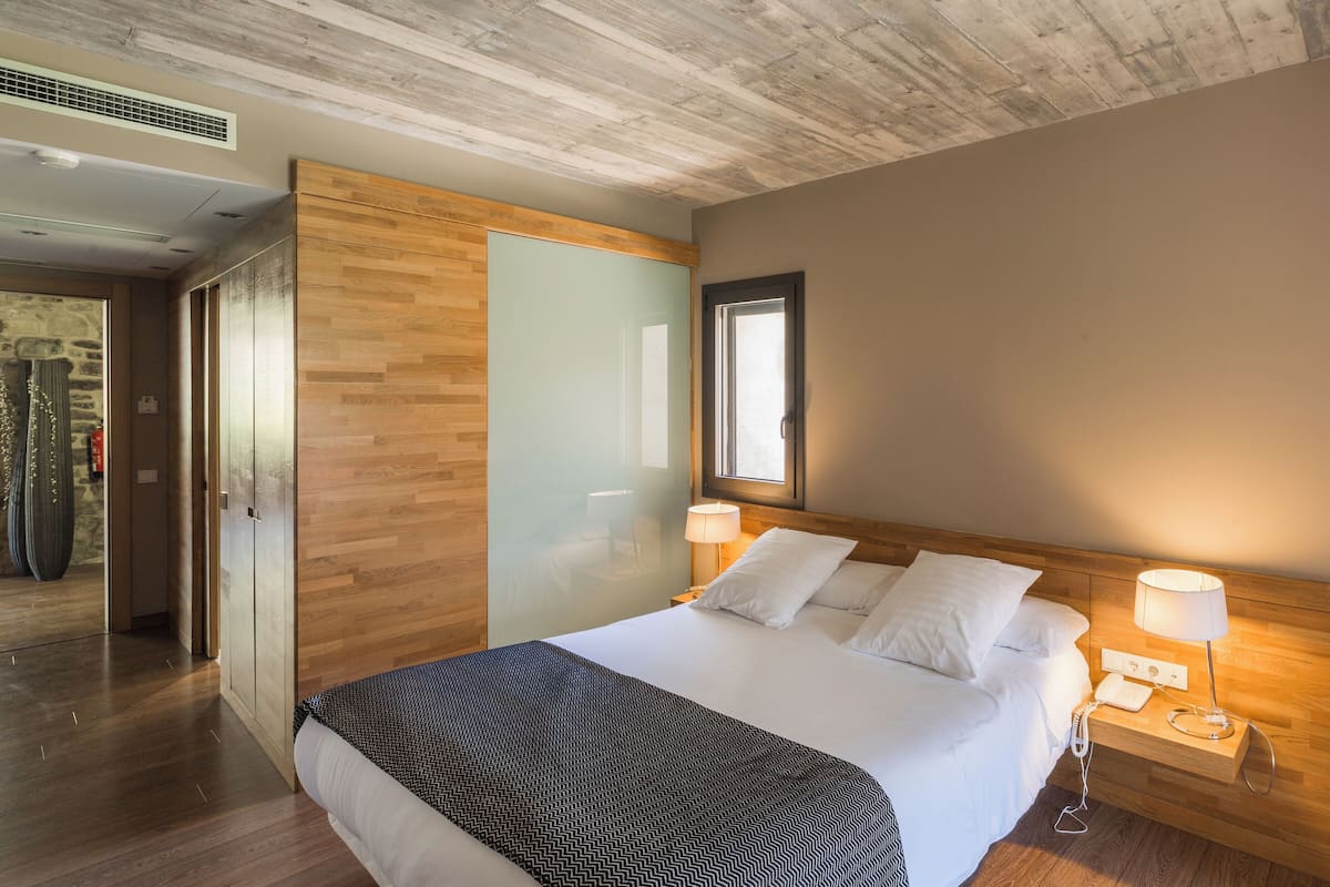 A hotel room with a wooden bed, two bedside lamps, a large mirror, and a stone wall.