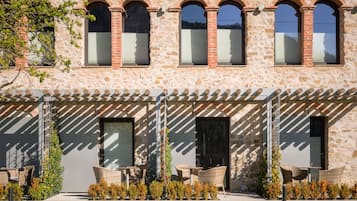 A stone building with arched windows and a covered outdoor seating area with wicker furniture.