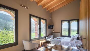 A bedroom with a large bed, a desk, a chair, and multiple windows offering a view of the outdoors.