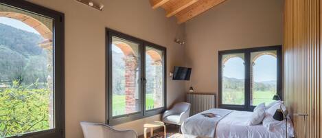 A bedroom with a large bed, a desk, a chair, and multiple windows offering a view of the outdoors.