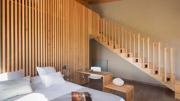 Un dormitorio moderno con un muro de listones de madera, una escalera de madera, una cama con ropa de cama blanca, un escritorio pequeño y una silla.