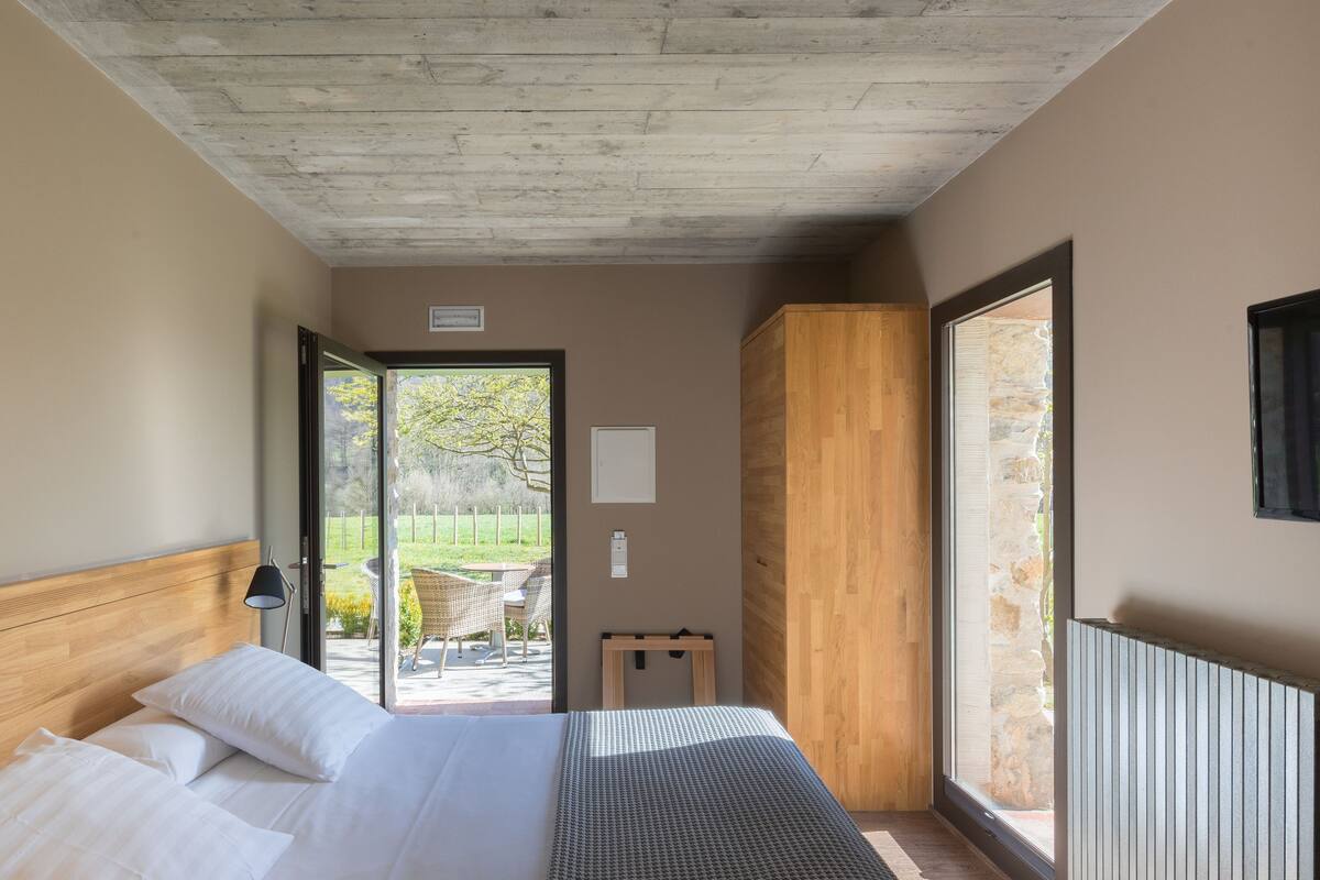 A bedroom with a bed, a TV, a wooden cabinet, and a view of the outdoors.