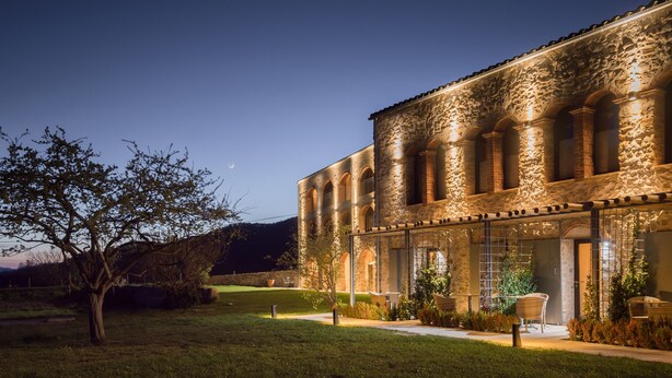 A stone building with arched windows and a well-lit exterior. - Les Planes del Grau (Sant Joan de Les Abadesses)