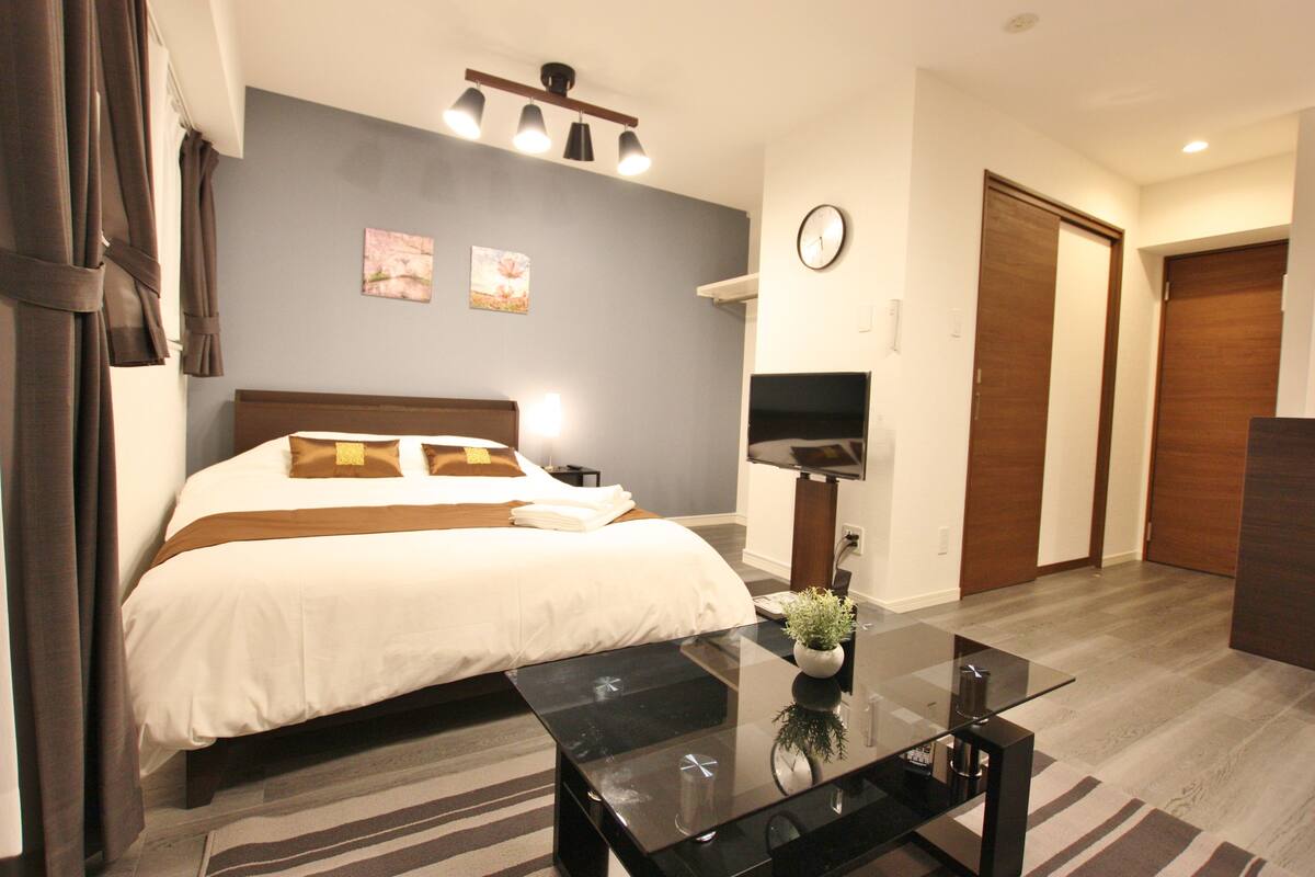 Una habitación de hotel con cama, televisor de pantalla plana, una mesita de centro y un reloj en la pared.