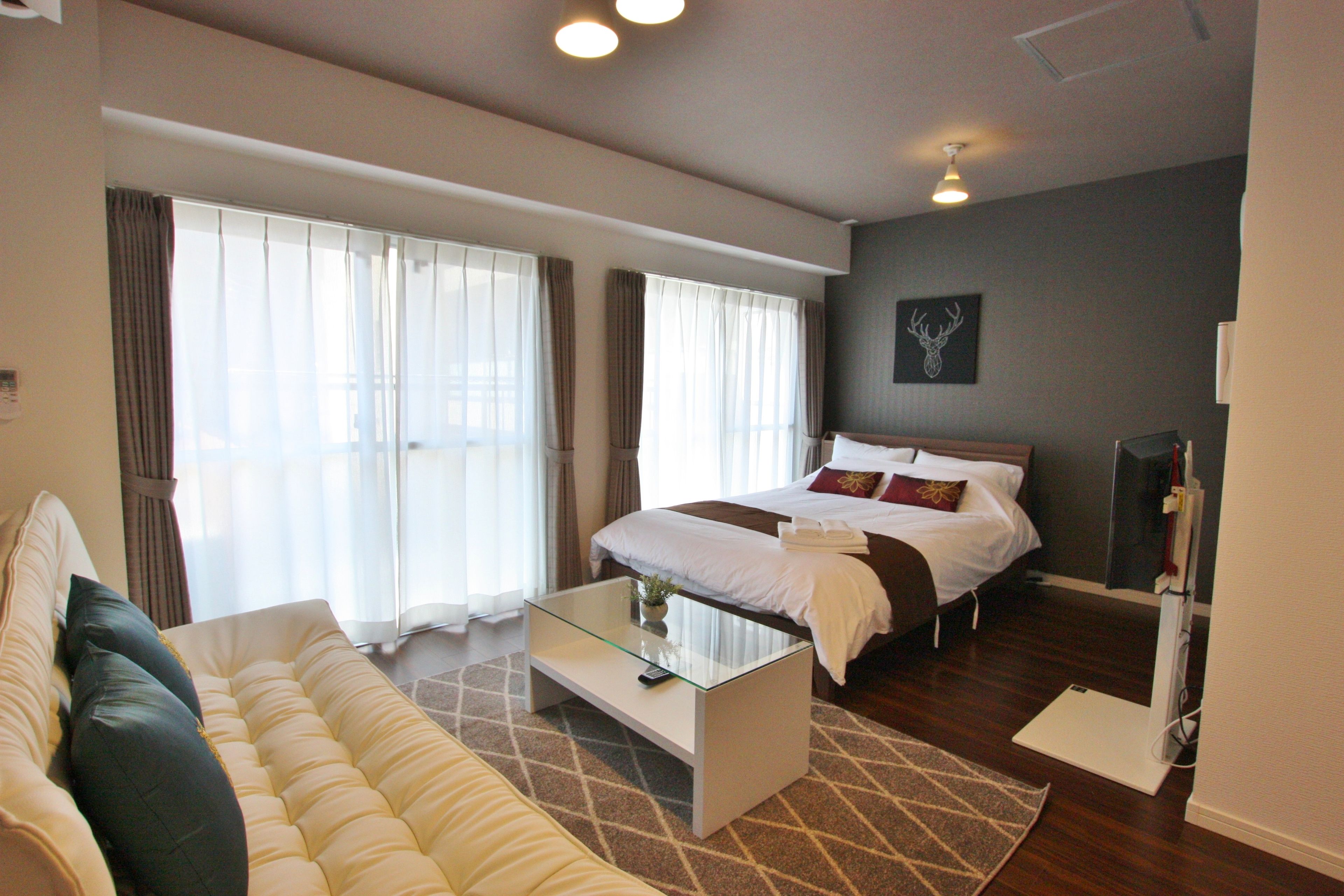 A hotel room with a bed, a sofa, a glass coffee table, and a large window with curtains.