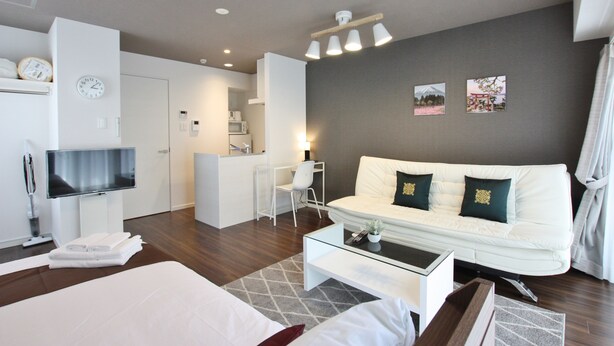 Ein modernes Hotelzimmer mit einem Bett, einem weißen Sofa, einem Couchtisch, einem Fernseher und einer kleinen Küchenzeile.