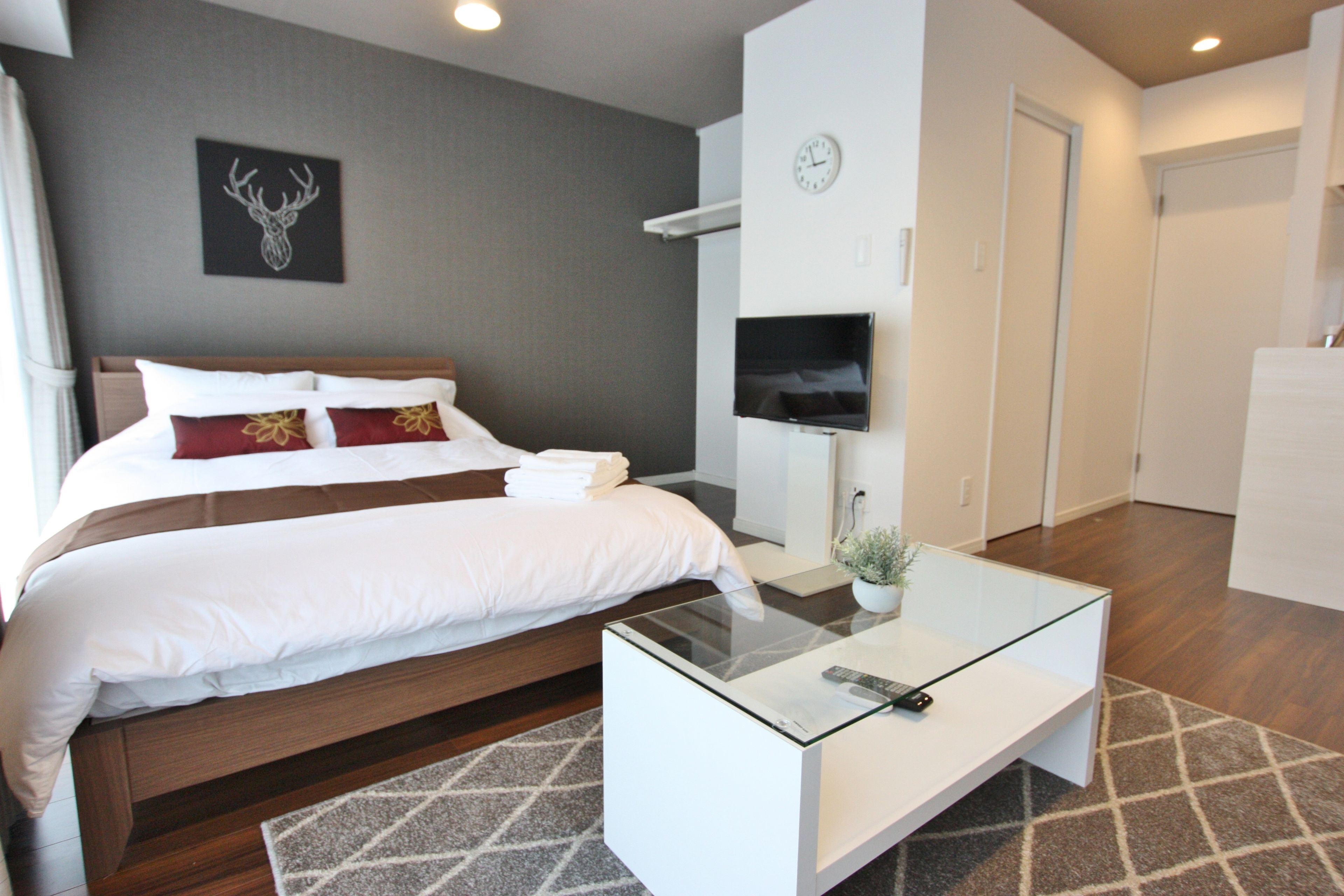 Una habitación de hotel moderna con una cama grande, una mesa de centro de cristal, un televisor y un reloj en la pared.