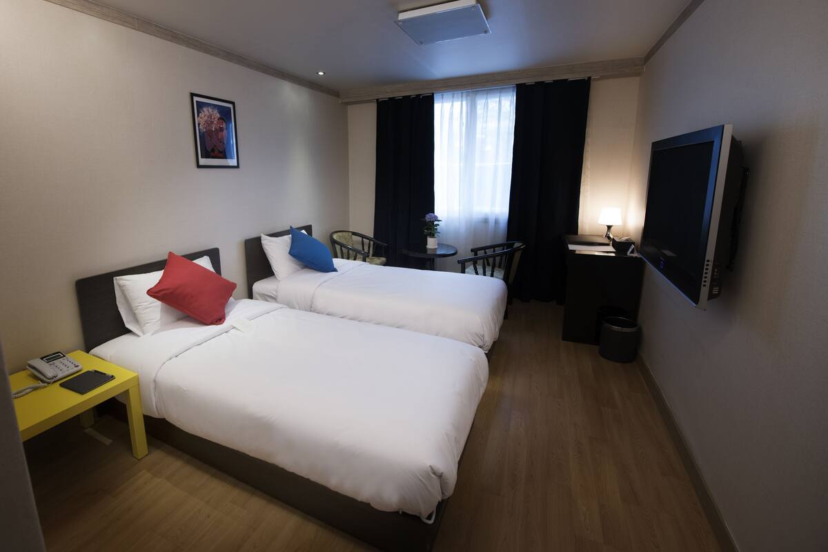 Habitación de hotel con dos camas, un escritorio, una silla, un televisor y una pequeña mesa con lámpara.