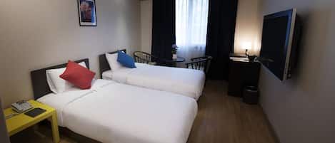 A hotel room with two beds, a desk, a chair, a TV, and a small table with a lamp.