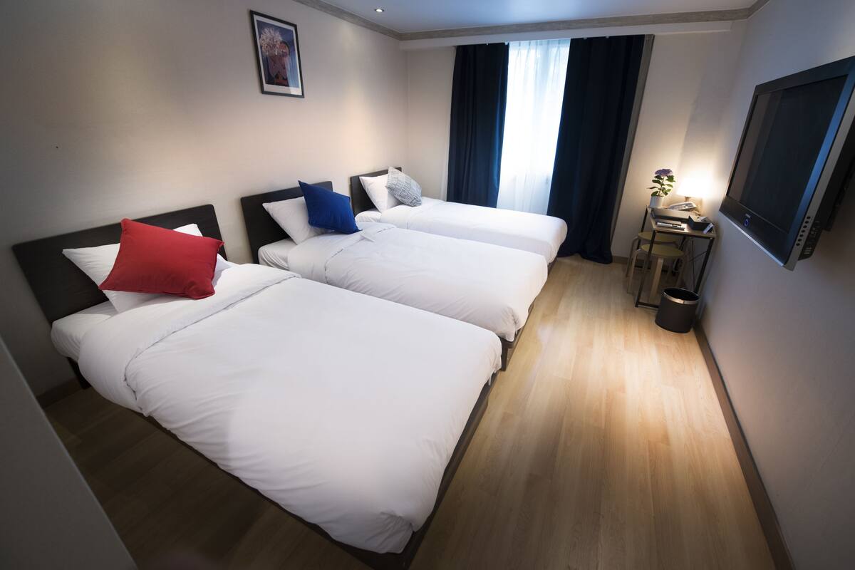 Habitación de hotel con dos camas, un escritorio con silla, televisor y ventana con cortinas.