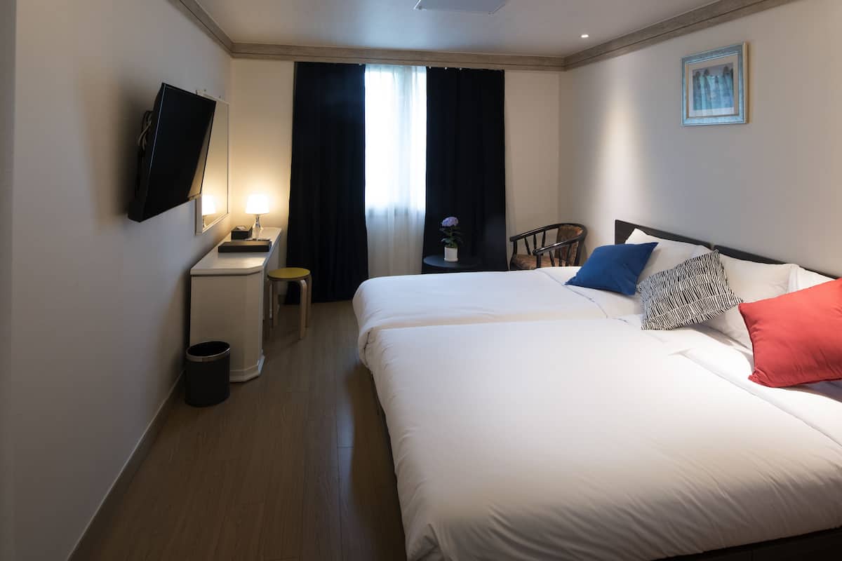 Habitación de hotel con cama, escritorio, silla, televisor y ventana con cortinas.